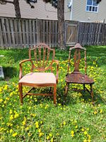 Front view of two antique chairs on grass: a shield back armchair with upholstered seat on left and dark wood side chair on right.