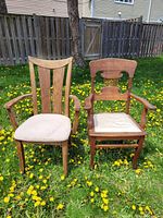 Front view of two wooden armchairs placed side by side on grass showing their design and cushioned seats.