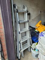 Folded aluminum extendable ladder leaning against a wall, surrounded by other items in storage.