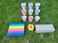 Lot laid out on grass showing flower pot stand with 12 ceramic pots, foam kneeling pad, metal mailbox, and sunflower grow kit.