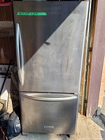 Photo of the fridge exterior showing stainless steel doors, bottom freezer drawer and handle with visible rust spots and sticker showing measurements