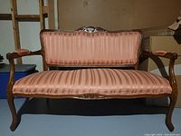 Front view of pink striped upholstery and carved wooden frame of the vintage duchess settee