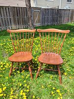 Pair of wooden Windsor chairs in a grassy outdoor setting with dandelions. Shows front view and side angles.