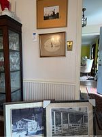 View of four framed scenic art prints including windmill, sailboat, historic house scenes hung on wall and resting against wall.