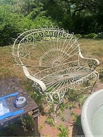 Vintage child-size metal settee with white paint and detailed scrollwork on a grass and brick patio.