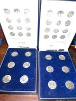 Two open coin cases showing 16 silver-toned cathedral coins in blue velvet inserts, with white lid interiors showing images and names of cathedrals.