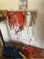 Photo showing assorted orange and white outdoor extension cords hanging and coiled on wooden beam and on floor with packaging visible on unopened 40ft cord.