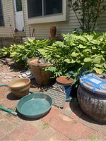 Photo showing multiple garden pots, garden hose coiled on ground, green shallow tray, and solar deck lights located outside a house with brick patio and plants.