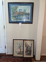 Three framed art pieces displayed: one hanging of cityscape, two leaning showing black and white prints.
