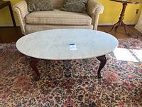 Full view of oval-shaped coffee table with white marble top and mahogany wood legs in a living room setting.