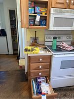 View showing kitchen cabinets and drawers open with plastic containers and wraps visible.
