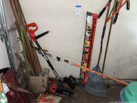 Black & Decker Edge Hog electric edger leaning against wall with rake and assorted wood pieces on floor