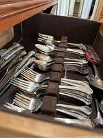 Drawer with arranged silver plated flatware including forks, spoons, and utensils in a brown felt tray.