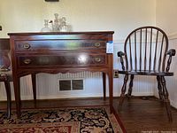 Vintage dark wood 2 drawer cabinet with brass drawer pulls and dark wood armchair beside it.