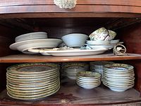 Bottom shelf of cabinet showing stacks of dinner plates, salad plates, and small bowls with dragon and phoenix motif.
