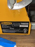 Detailed close-up of Workforce tile cutter model plate, showing model THD550, specifications, serial number, and warning label.
