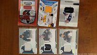 12 assorted hockey jersey trading cards shown face up on table with clear visible jersey fabric swatches in each card.