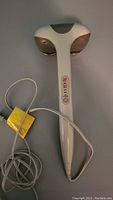 Front view of the white and gray handheld massager wand with control buttons on the handle and attached power cord.