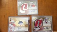 Three hockey rookie cards with patches and autographs, laid out on a wooden surface and protected in plastic cases.