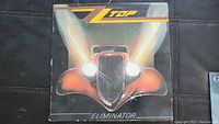 Front cover of ZZ Top Eliminator vinyl album showing a red stylized hot rod car with headlights on a dark background