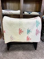 Quilt displayed folded over a wooden stand showing original multi-colored patterns in red, turquoise, and pink on white background with visible hand quilted stitching.