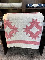 Front side of the quilt draped over a wooden stand, showing the pink and white Hands All Around pattern with stitching detail.