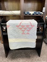 Quilt with pink basket patterns draped over a wooden quilt rack in a room with other folded quilts on shelves.