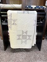 Ohio Star quilt folded over a black wooden rack showing hand pieced star patterns and wear.
