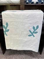 Front view of the quilt draped over a stand showing white background with blue leaf stems on corners and sides.