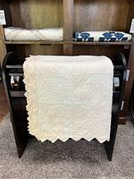 Front and sides view of the pink 1920 hand made prairie point quilt draped over a dark wood rack showing the distinctive scalloped edges and patchwork quilting.