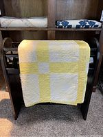 Full quilt displayed folded over a dark wood quilt stand showing the Yellow Star design in soft yellow and off-white fabrics.