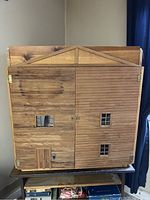 Closed view of large handmade wooden dollhouse with small windows and porch door details.