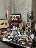 Photo showing wide view of the lot on a table, including wooden hat forms, framed art, irons, spools, and crocks