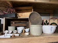 Grey Coors crock with wooden lid at center, white porcelain mortars and pestles in front, wicker bag and oval bowl at right