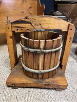 Front view of antique wooden grape press showing cylindrical basket, metal bands, wooden frame and screw mechanism.