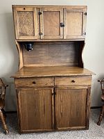 Frontal view of the antique wooden Hoosier cabinet showing the upper and lower sections, both with panel doors and dark hardware.