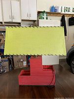 Lamp showing side with yellow rectangular shade with black braided trim and red planter base divided into two sections.