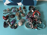 Photo showing mixed fashion jewelry laid out including earrings, rings, pendants, and bracelets on a surface with a blue and white background.
