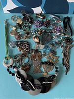 Mixed lot of owl-themed pins and necklaces spread on blue surface showing various metal tones and designs including leaf shapes and floral motifs.
