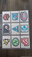 Front side of nine 1977 OPC hockey team cards showing various NHL team logos in colorful designs, arranged in a 3x3 plastic sleeve.