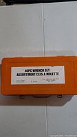 Closed orange hard plastic case with a label stating '40PC WRENCH SET ASSORTIMENT CLES A MOLETTE'.