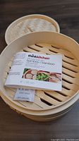 Photo of the bamboo steamer with lid off, showing label and slatted bottom tray inside.