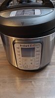 Front view of Instant Pot showing digital display and control buttons with stainless steel body and black lid.