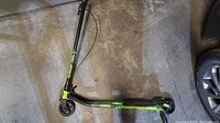 Side view of the Madd Gear X-Karver scooter showing black frame with green highlights and rear brake