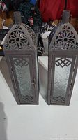 Pair of two dark metal outdoor candle lanterns with domed tops and frosted glass panels on white surface.