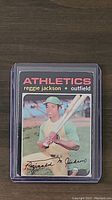 Front view of 1971 Topps Reggie Jackson card showing him in Athletics uniform holding bat, card encased in plastic protective sleeve.