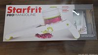 Box of Starfrit Pro Mandoline shows slicer with safety holder and blade.
