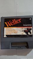Closed gray plastic carrying case with Weller logo sticker and product information on the lid, showing brand and model info.