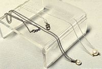 Two sterling silver necklaces displayed on clear acrylic stand, showing chain length difference and pearl pendants.