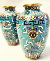 Front view of one vase showing turquoise enamel and floral cloisonné motifs, second vase blurred in background